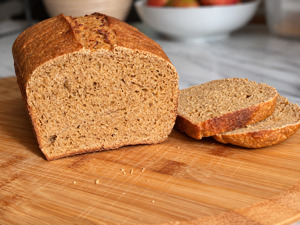 Golden-brown loaf of bread with two slices on a wooden cutting board.